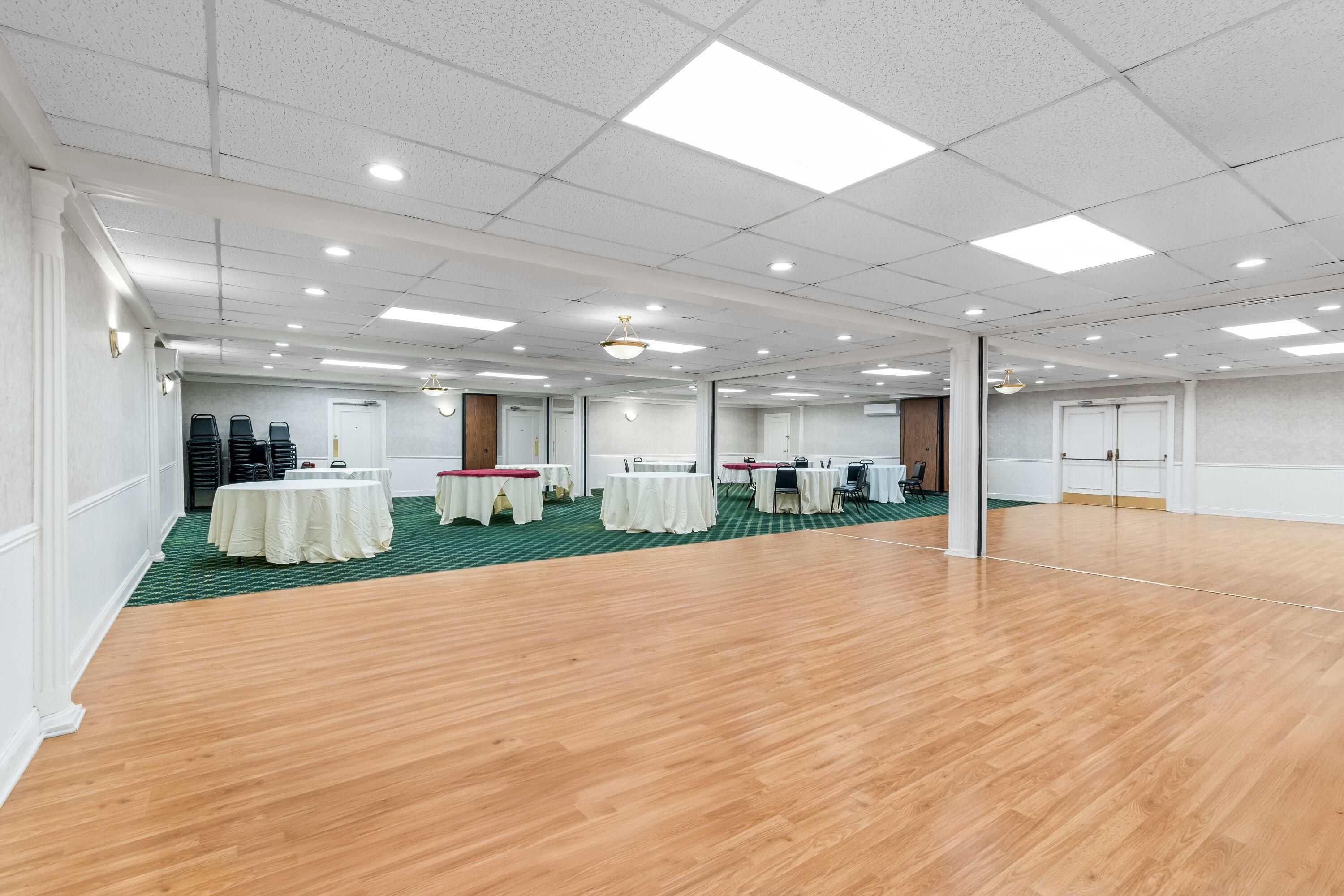 Un amplio salón de conferencias con varias mesas y sillas, suelo de madera y un techo alto con iluminación empotrada.