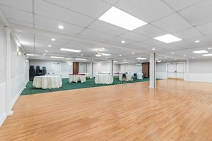 Un amplio salón de conferencias con varias mesas y sillas, suelo de madera y un techo alto con iluminación empotrada.