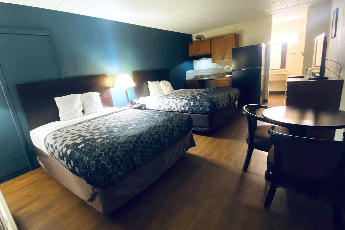 Une chambre d’hôtel avec deux lits, un bureau, une chaise, un réfrigérateur et une kitchenette.