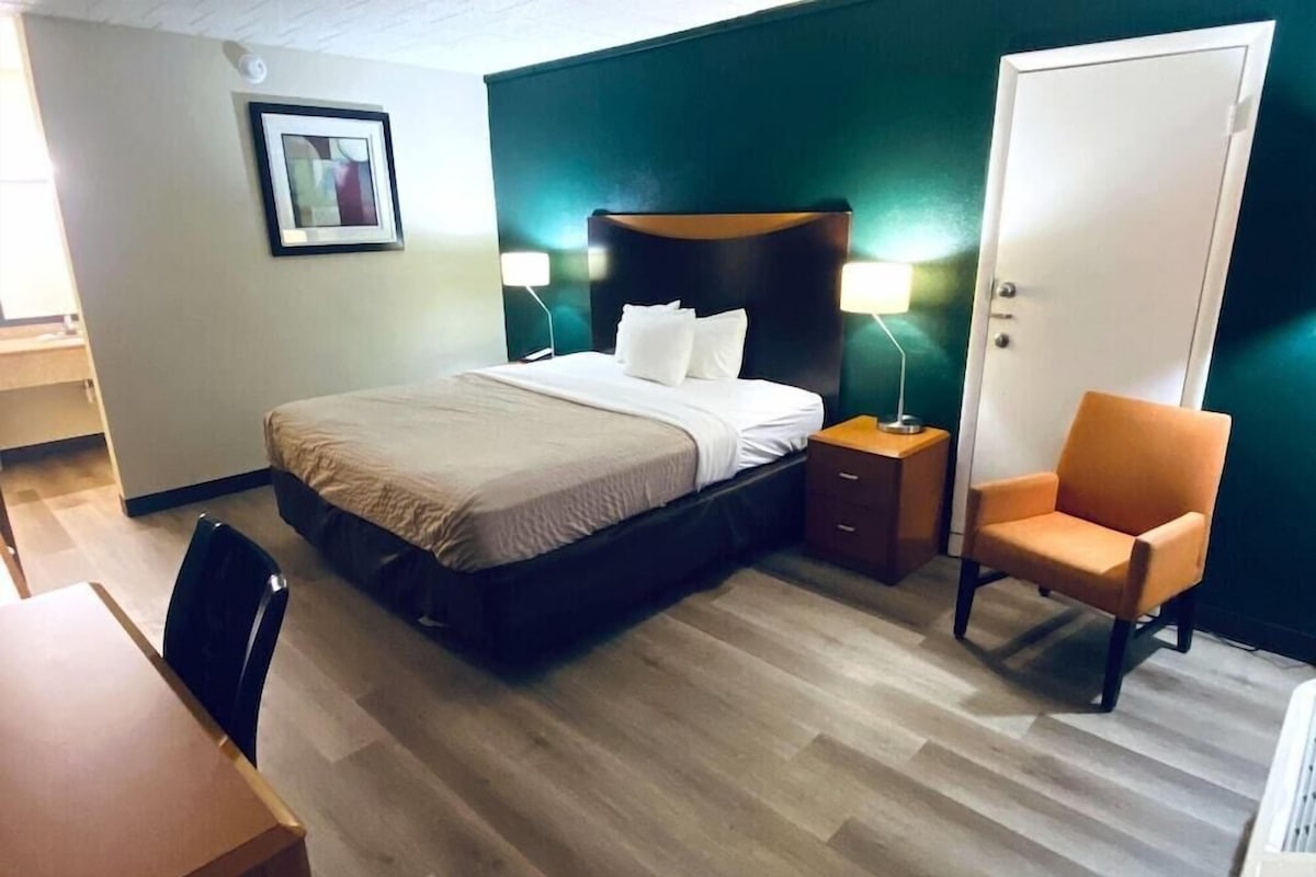 Une chambre d’hôtel avec un lit, une table de chevet, une chaise et une porte.