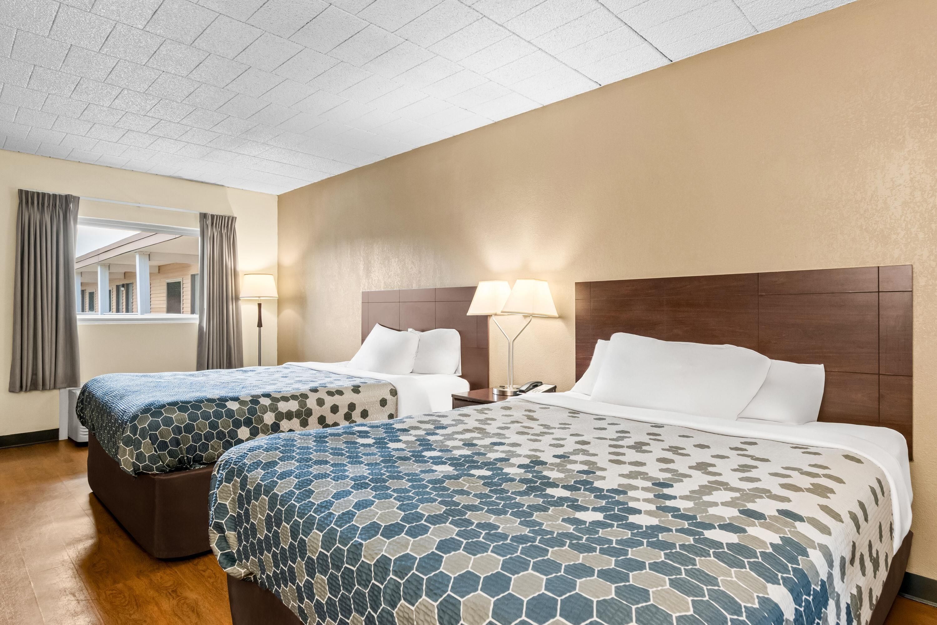 Habitación de hotel con dos camas, una ventana con cortinas, una lámpara y vistas al exterior.