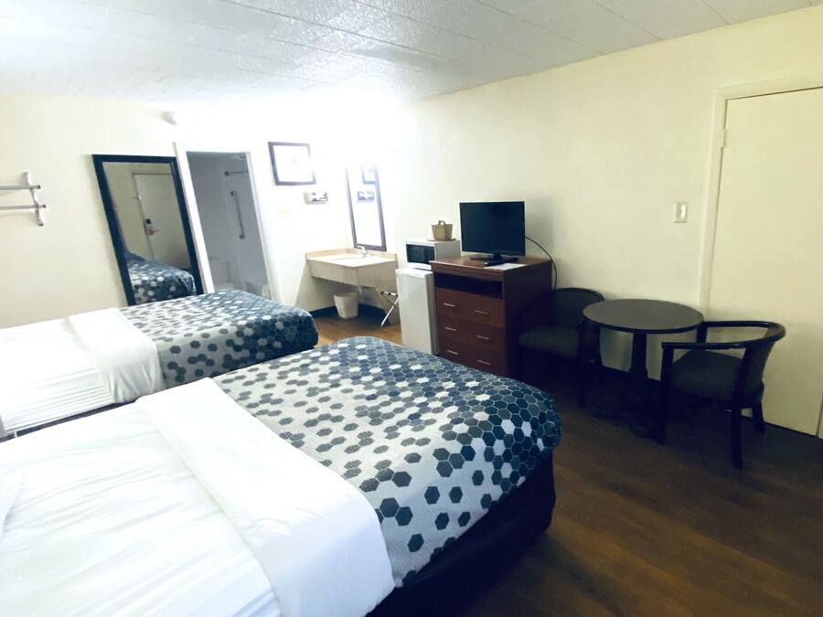 A hotel room with two beds, a desk with a computer, a chair, a small table, and a door.