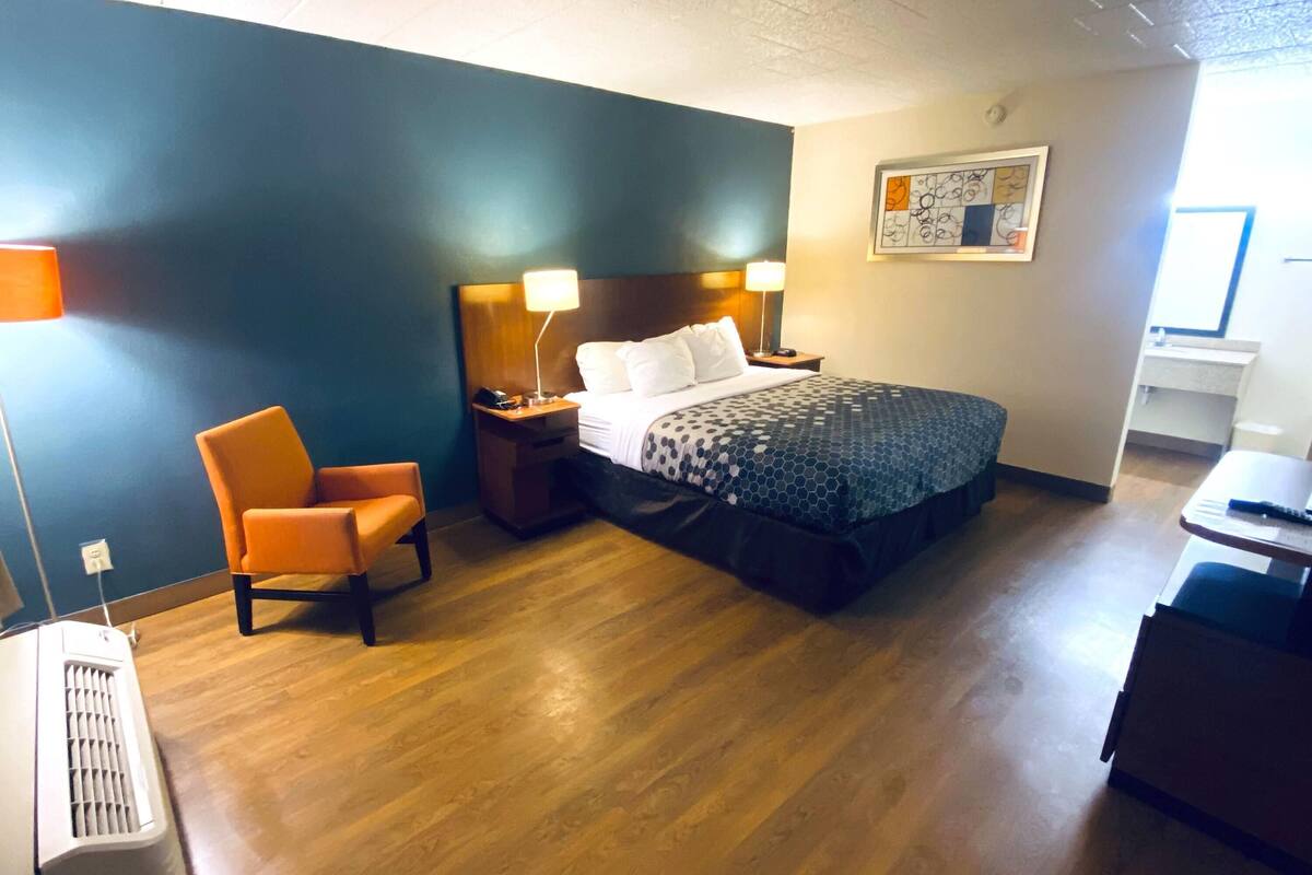Une chambre d’hôtel avec un lit, une chaise orange, une table de chevet, une lampe et un radiateur.