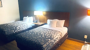Ein Hotelzimmer mit zwei Betten, einem Nachttisch, einer Lampe und einer Steckdose.