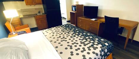 A hotel room with a bed, a desk, a television, a microwave, and a refrigerator.