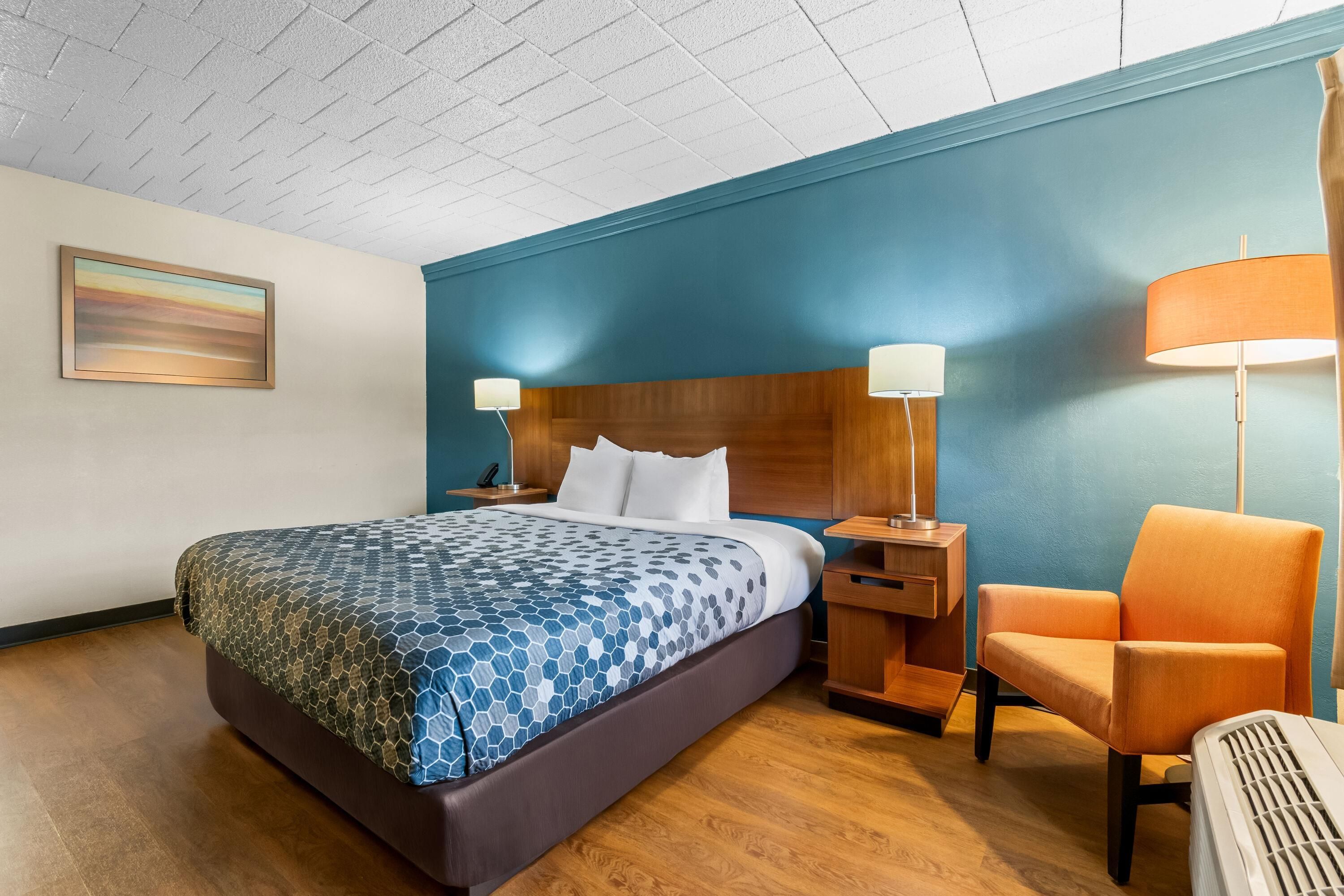 A hotel room with a bed, a chair, a nightstand, and a lamp.