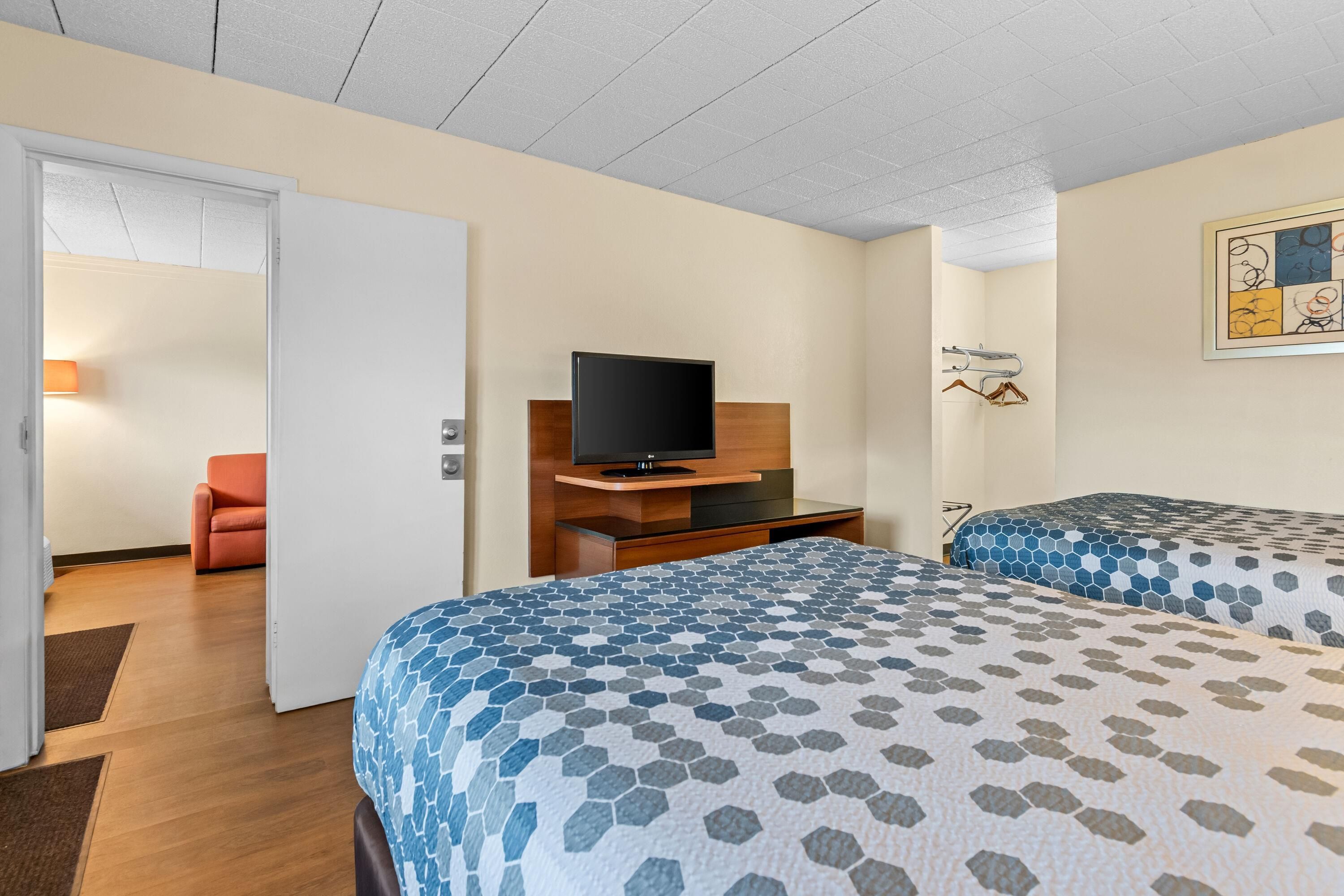 A hotel room with two beds, a TV, a desk, and a door leading to another room.