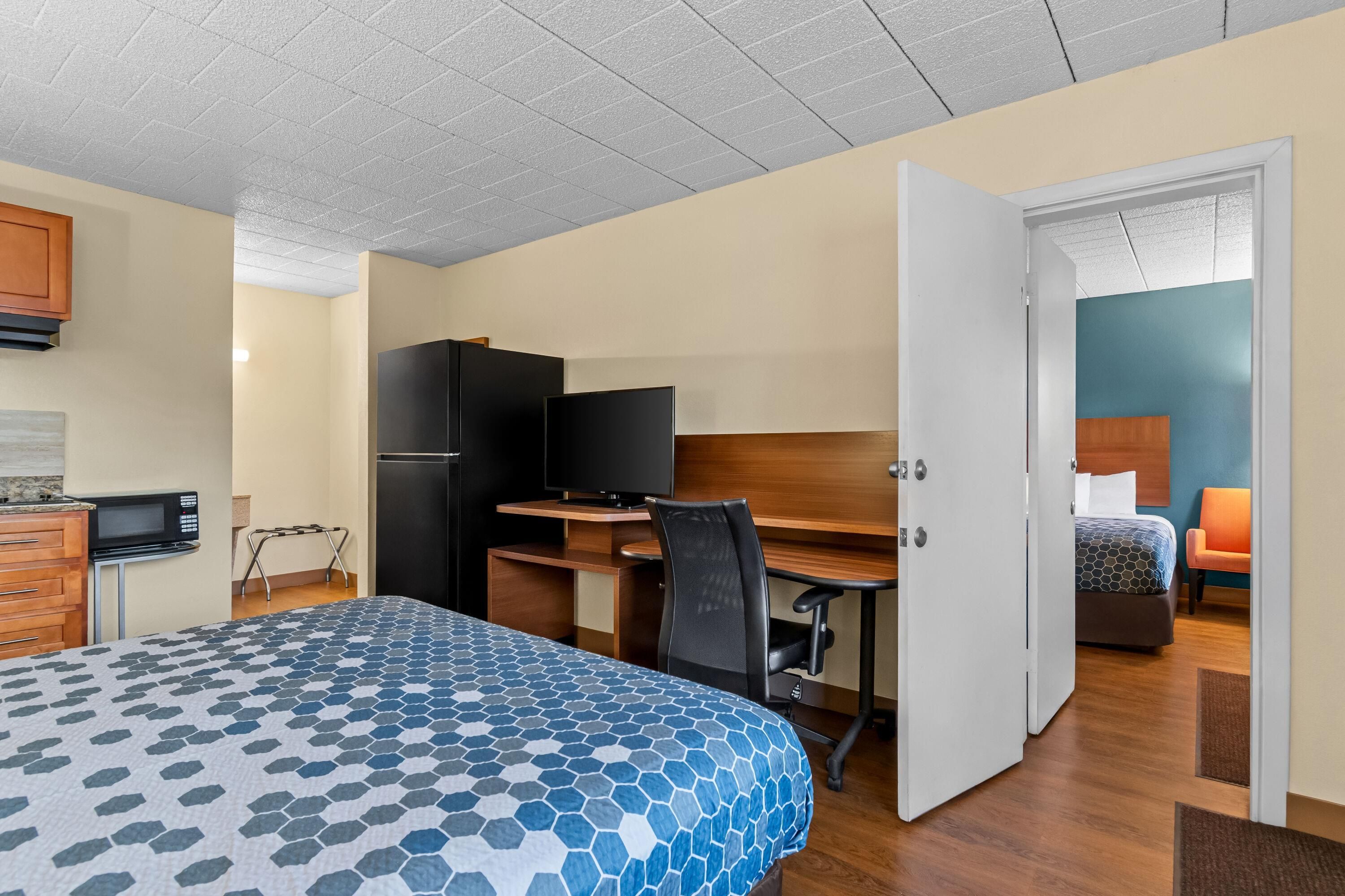 Et hotelværelse med seng, skrivebord med computer, fjernsyn og tekøkken.