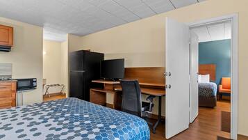 A hotel room with a bed, a desk with a computer, a television, and a kitchenette.