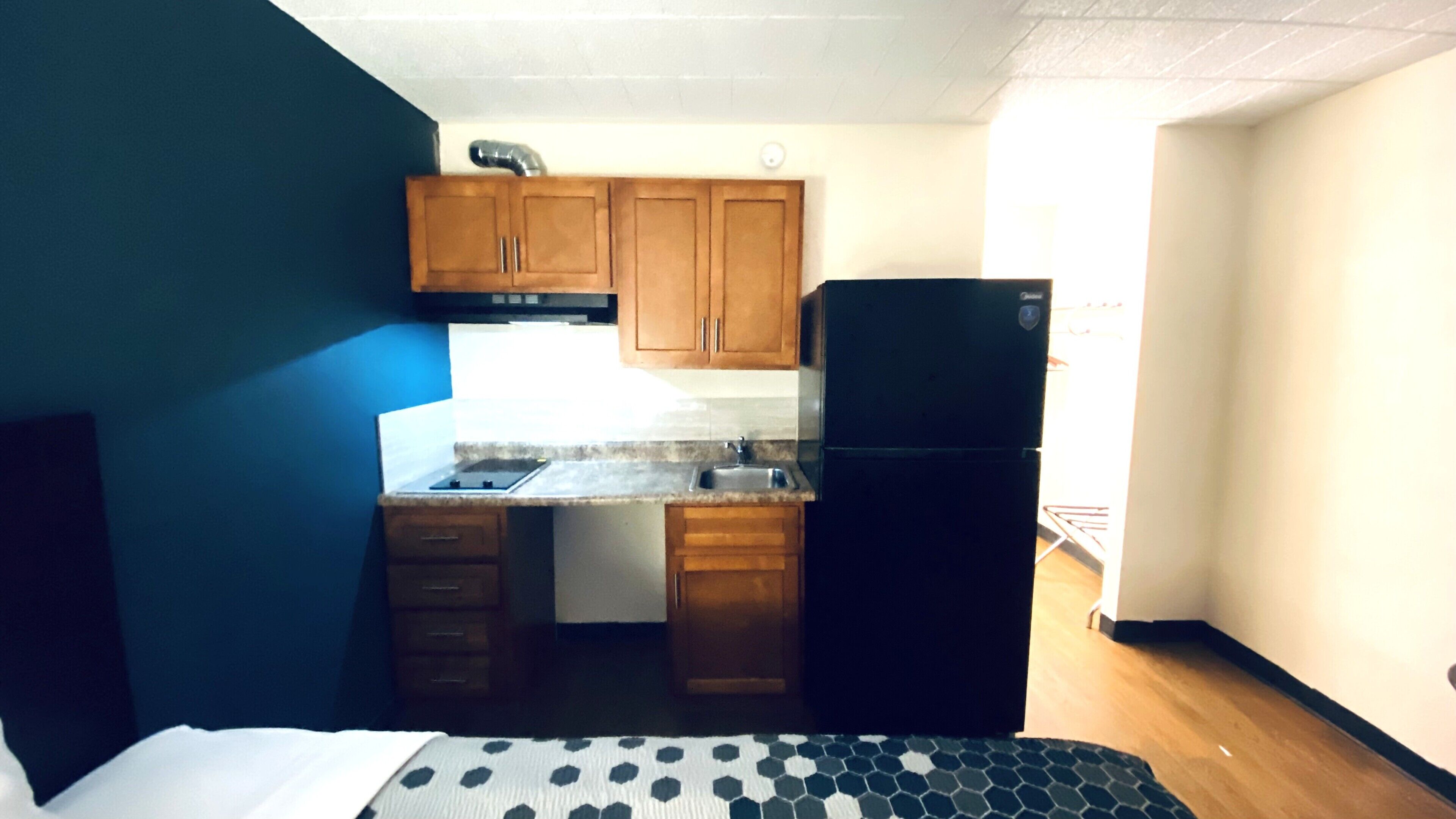 A compact kitchen with wooden cabinets, a black refrigerator, and a small countertop.