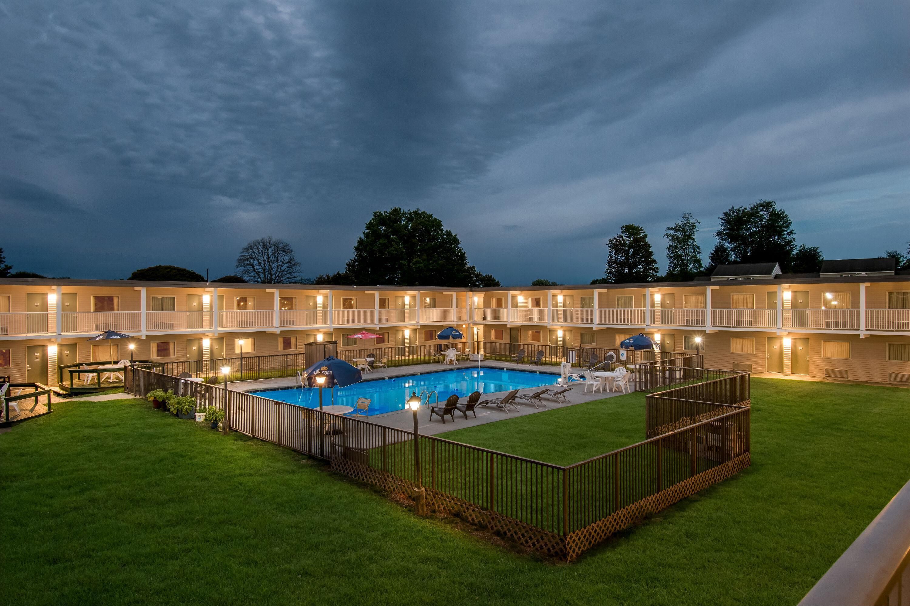 Un hotel amb una piscina envoltada per una zona tancada, diversos balcons i seients a l'aire lliure.