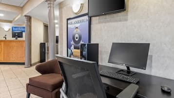 Un mostrador de recepción con una computadora, un monitor y una silla. Hay un cartel en la pared y un televisor sobre el mostrador.
