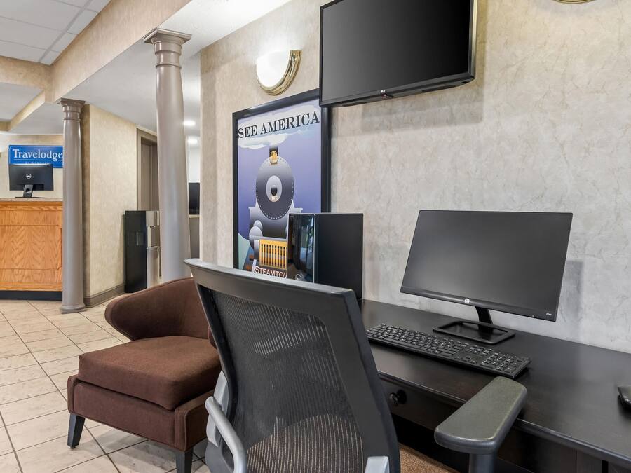 Un mostrador de recepción con una computadora, un monitor y una silla. Hay un cartel en la pared y un televisor sobre el mostrador.