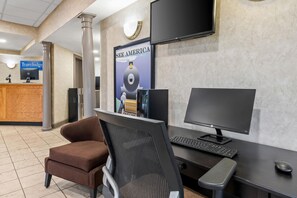 A reception desk with a computer, a monitor, and a chair. There is a poster on the wall and a television above the desk. - Travelodge by Wyndham Shamokin Dam/Selinsgrove (Shamokin Dam)