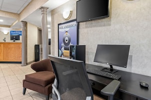 Un mostrador de recepción con una computadora, un monitor y una silla. Hay un cartel en la pared y un televisor sobre el mostrador.