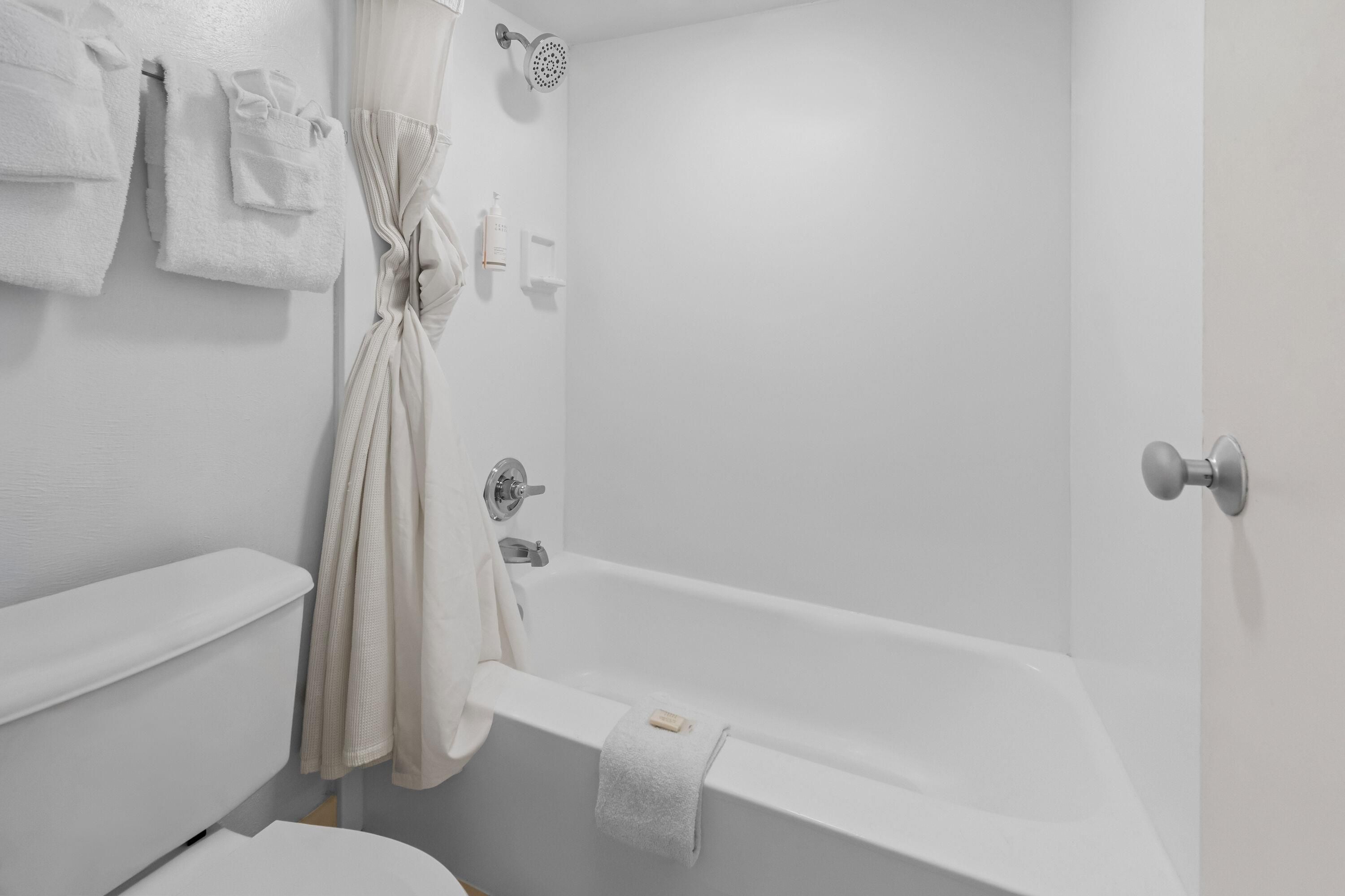 A bathroom with a bathtub, toilet, and a towel rack with towels.