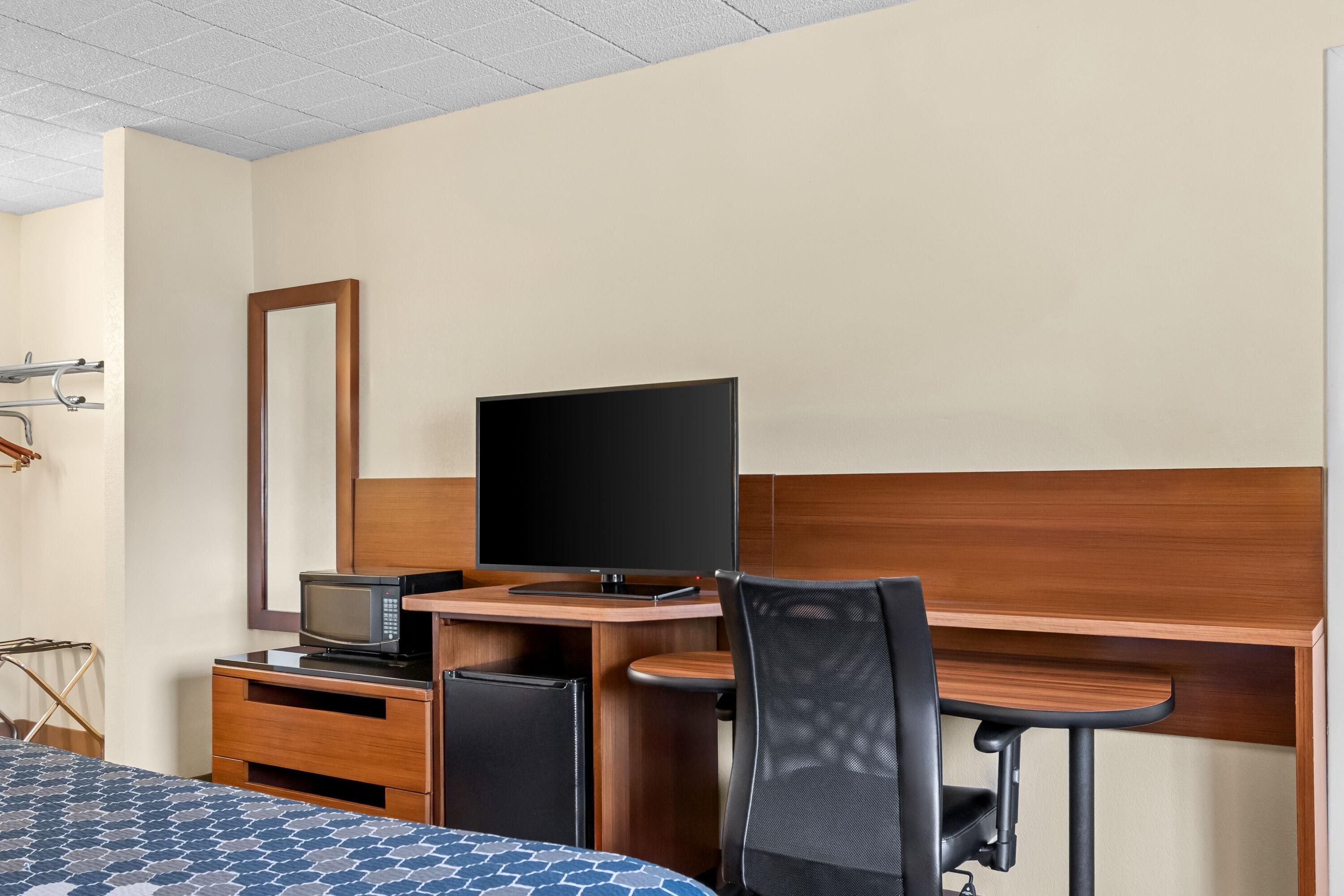 A hotel room with a bed, a desk with a computer, a television, and a mirror.