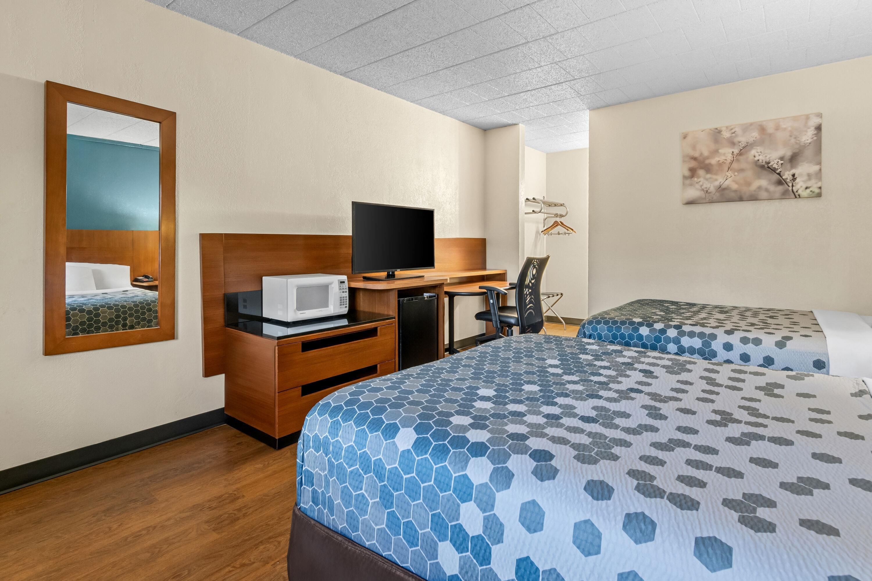 A hotel room with a bed, a desk with a computer, a microwave, a chair, and a TV.