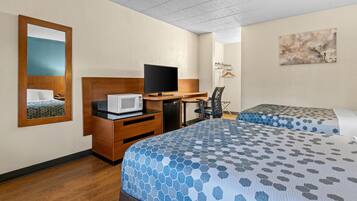 A hotel room with a bed, a desk with a computer, a microwave, a chair, and a TV.
