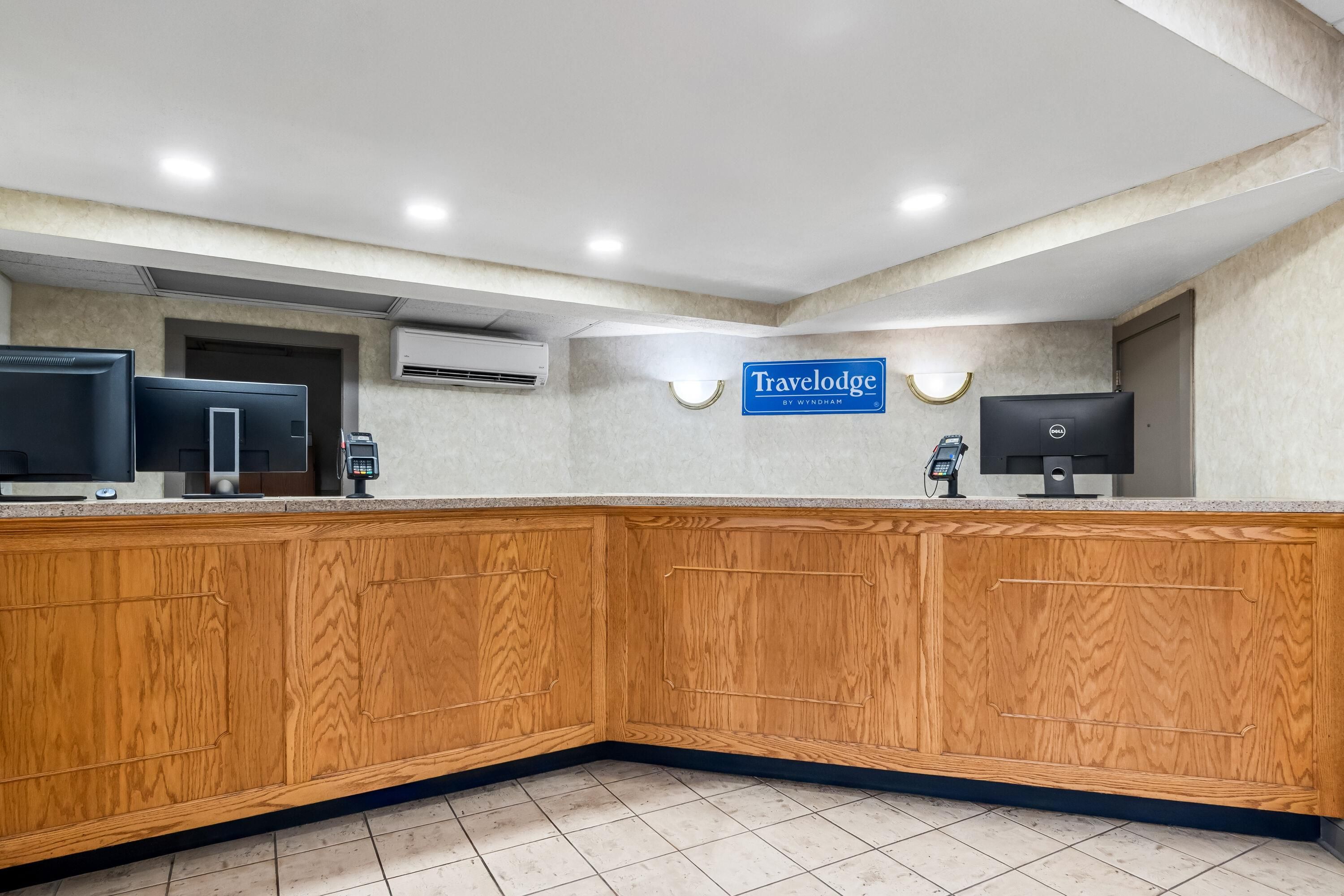 A reception area with a wooden counter, a sign for Travelodge by Wyndham, and a Dell computer.