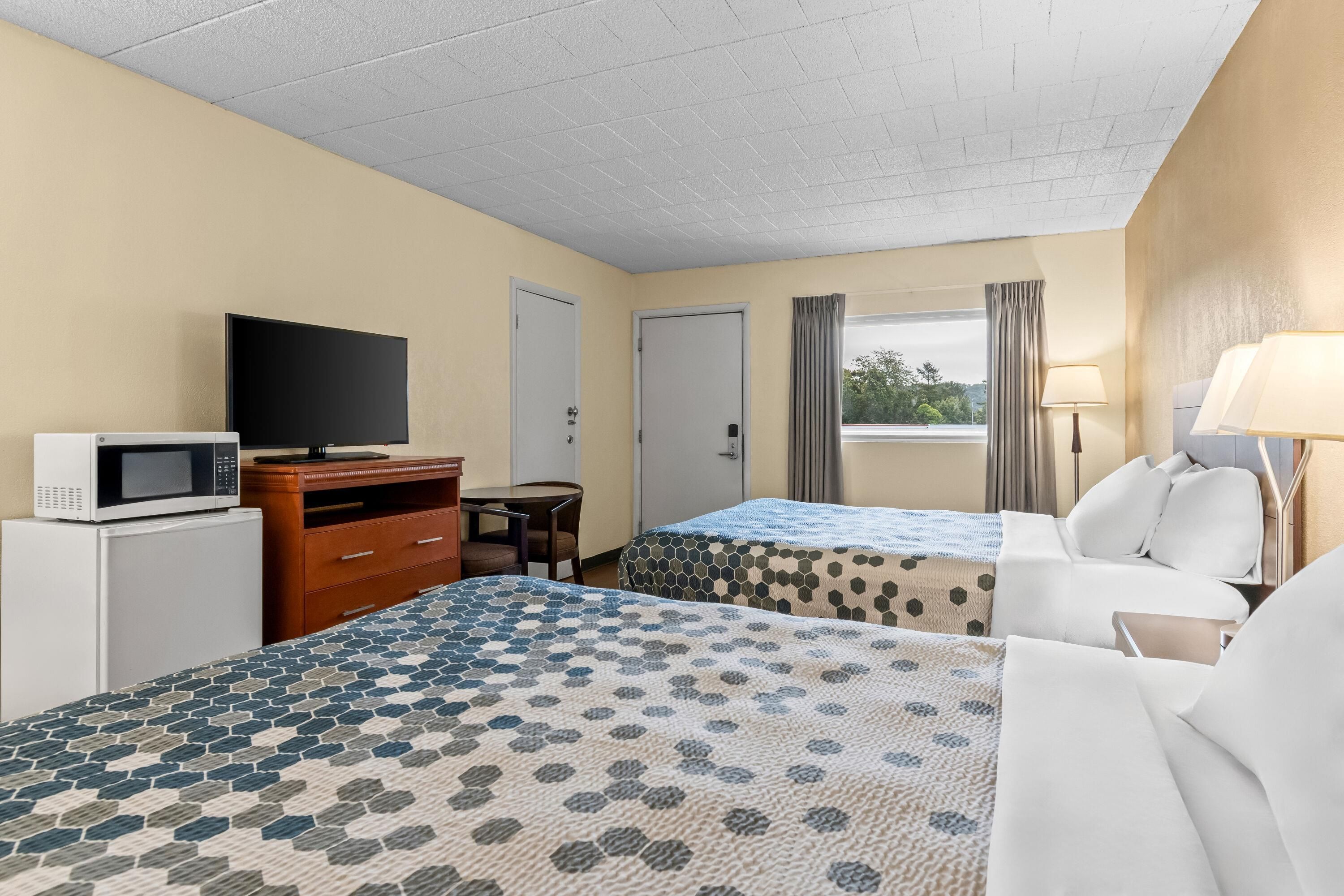 Una habitación de hotel con dos camas, un escritorio con televisor, microondas y una ventana con cortinas.