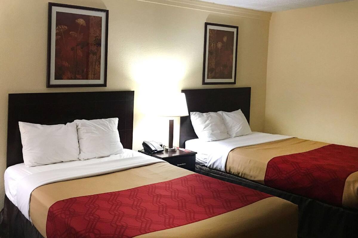 Une chambre d’hôtel avec deux lits, une table de chevet avec un téléphone et deux tableaux encadrés au mur.