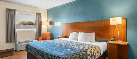 Habitación de hotel con una cama grande, dos lámparas de noche, un ventanal con cortinas y vistas a árboles.
