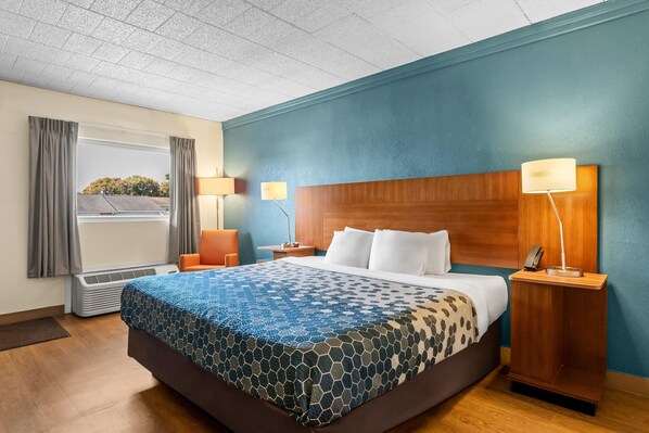 A hotel room with a large bed, two bedside lamps, a window with curtains, and a view of trees.