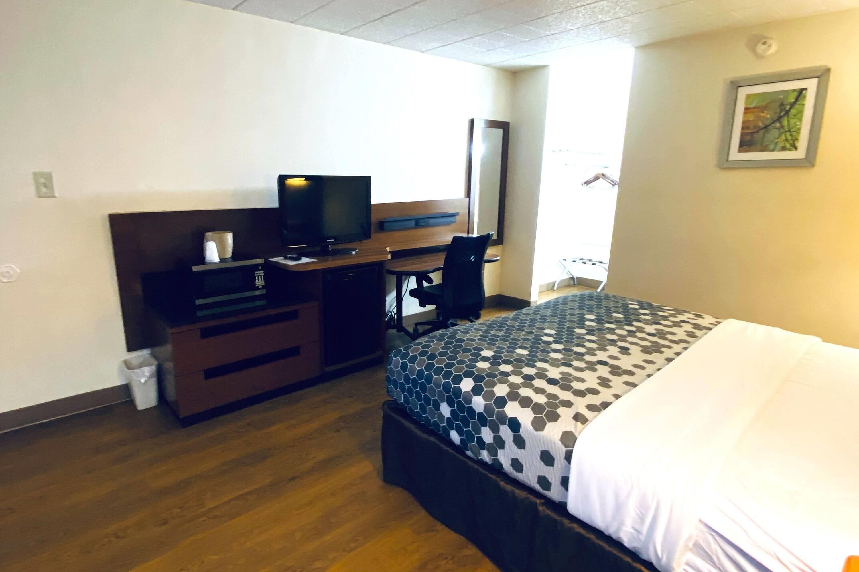 A hotel room with a bed, a desk with a computer, a chair, and a television.