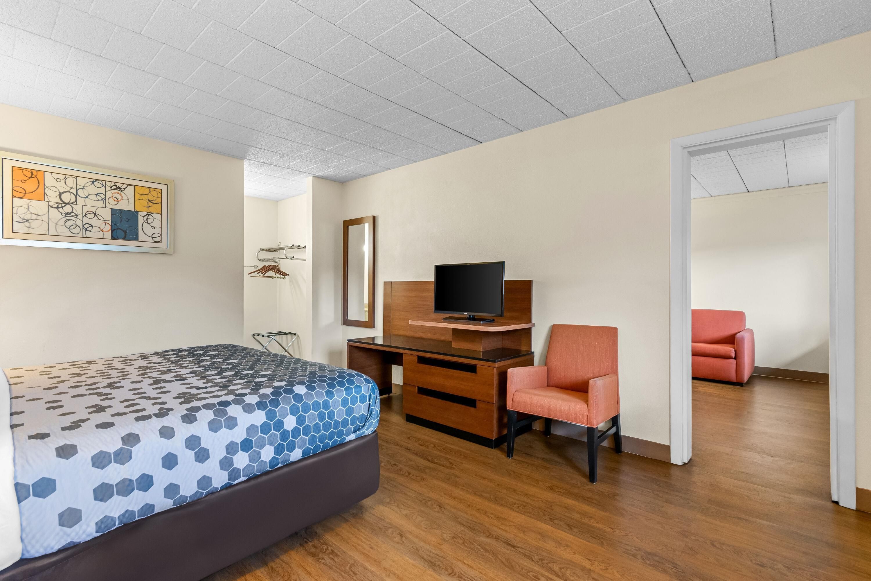 A hotel room with a bed, a desk with a TV, a chair, and a red sofa.