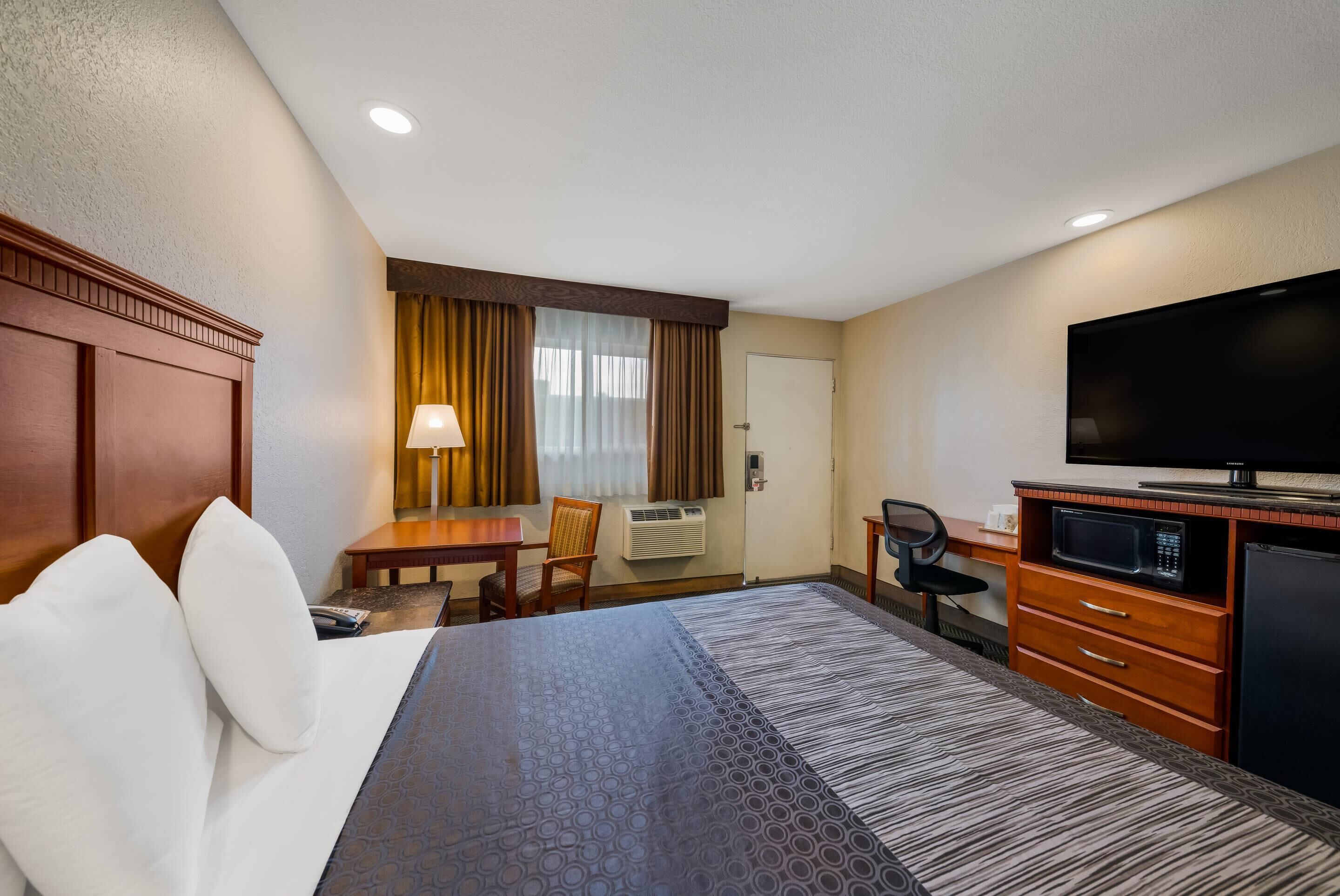 Una habitación de hotel con cama, escritorio, silla, televisor y microondas.