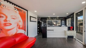 A hotel reception area with a modern design, including a reception desk, a red seating area, and a wall with a large postage stamp. - Rodeway Inn South San Francisco Airport (South San Francisco)