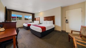 A hotel room with two beds, a desk, a chair, and a view of the outside. - Rodeway Inn South San Francisco Airport (South San Francisco)