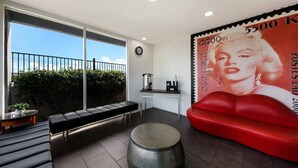 A modern living area with a large window, a red couch, a round table, and a wall-mounted clock. - Rodeway Inn South San Francisco Airport (South San Francisco)