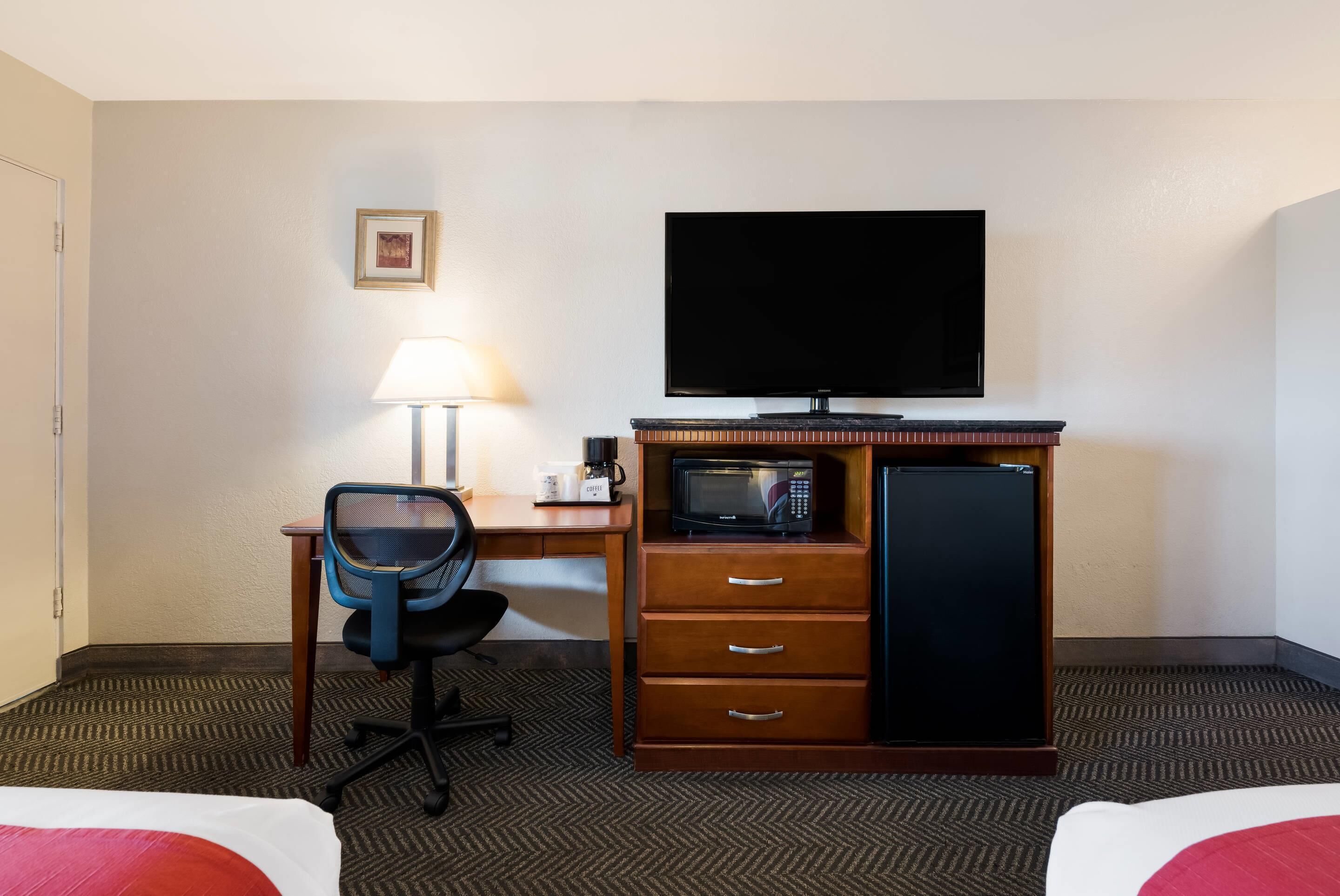 A hotel room with a bed, a desk with a chair, a television, a microwave, and a refrigerator.