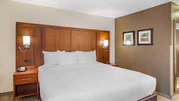 A hotel room with a large bed, wooden headboard, two bedside tables with lamps, a phone, and two framed pictures on the wall.