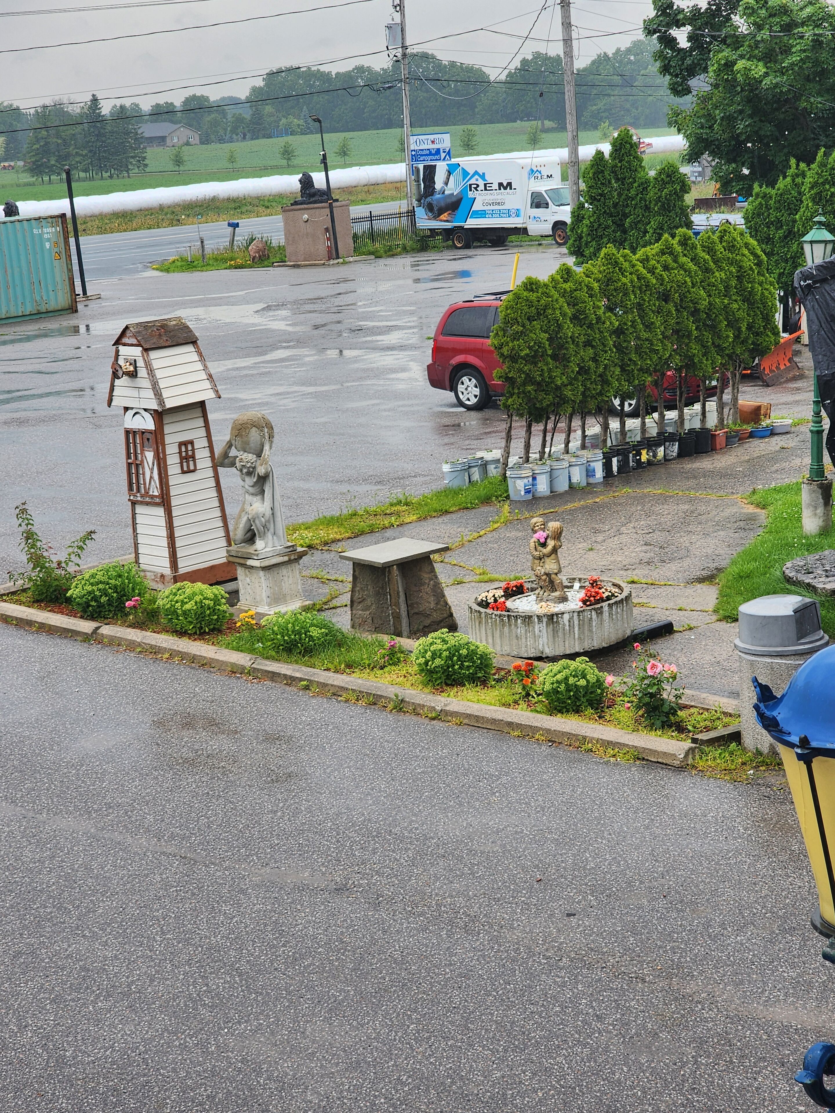 Un parcheggio con una statua di un uomo e un uccello, circondato da vegetazione e un piccolo stagno con fiori.