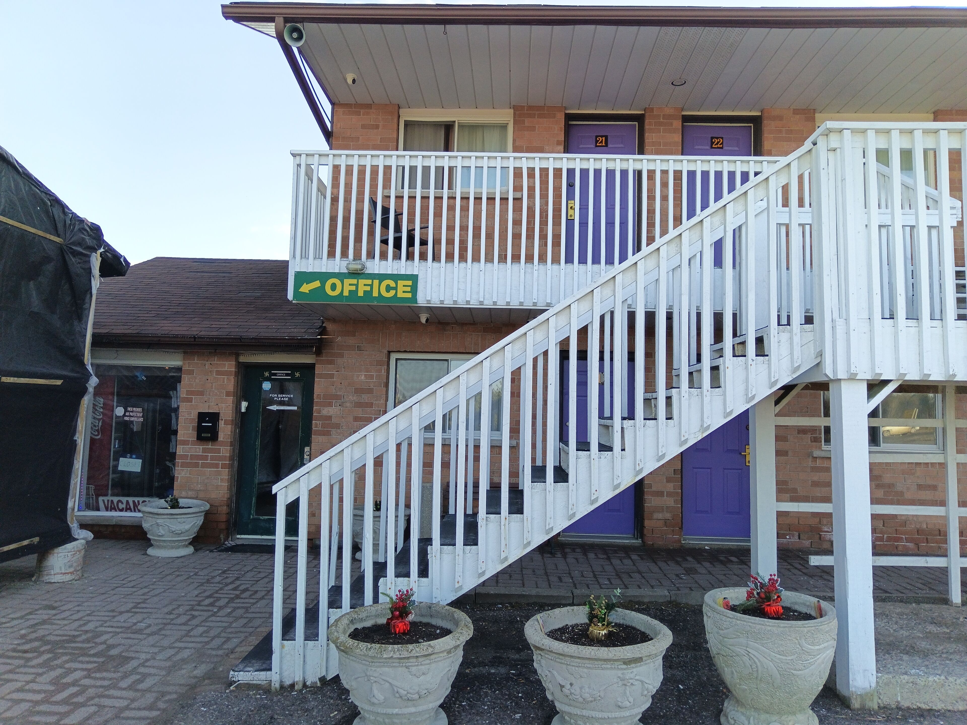 A building with a staircase leading to a balcony, a sign indicating an office, and three potted plants.