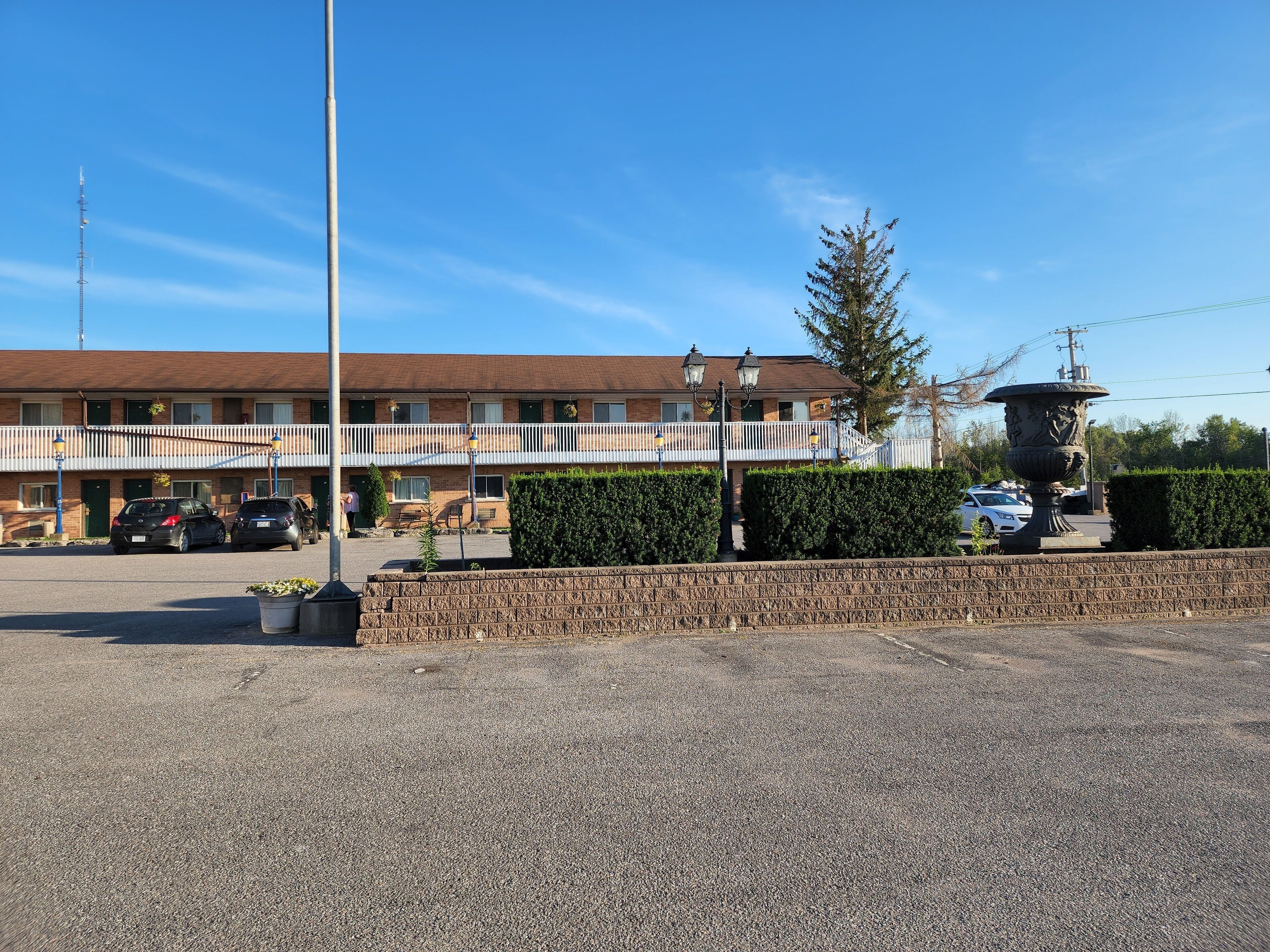 Un motel de dos pisos con balcón, estacionamiento y una urna decorativa.