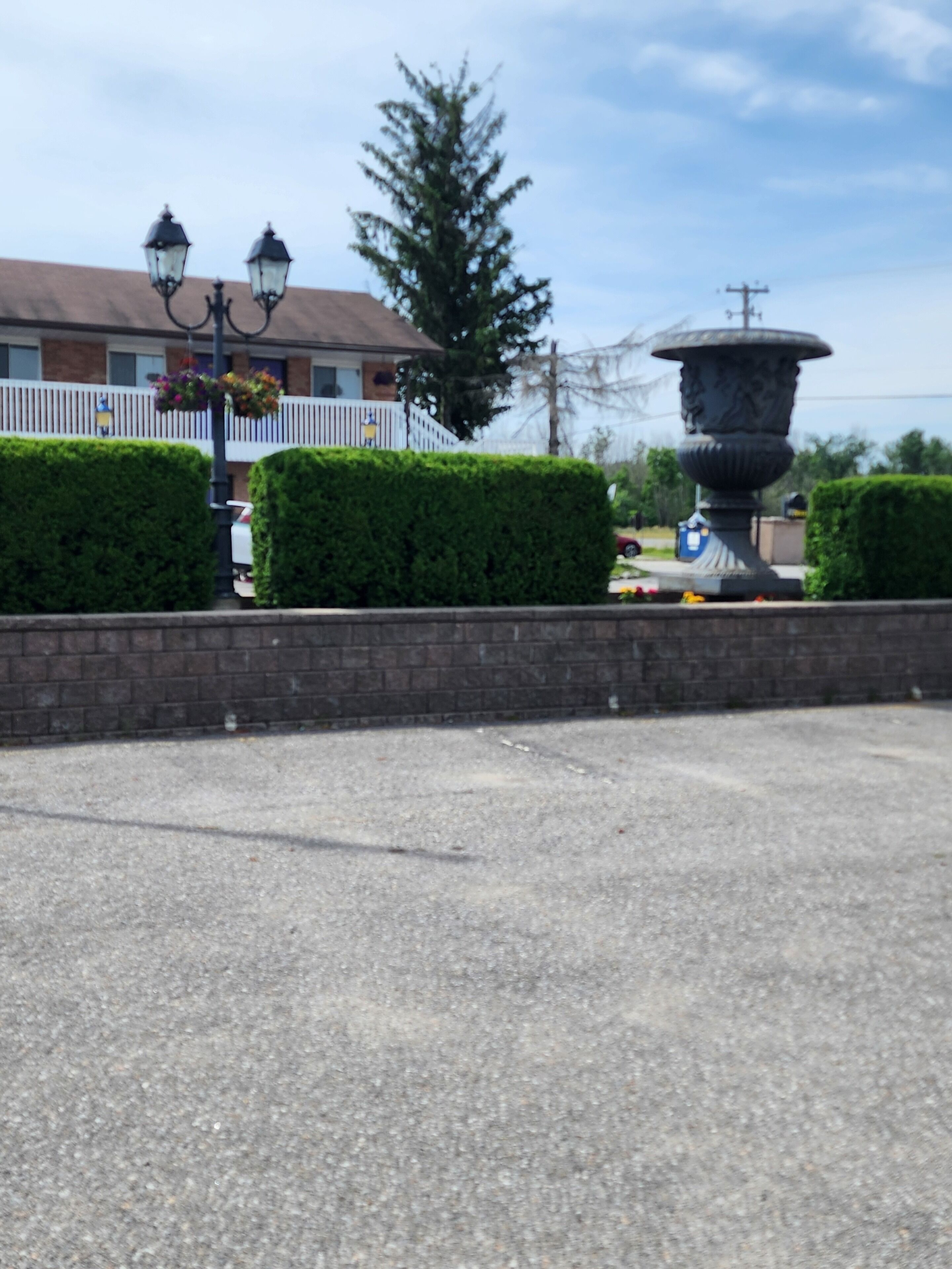 A parking lot with a decorative fountain, neatly trimmed hedges, and a building with a white fence in the background.