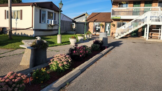 A row of mobile homes with a grassy area in between, a small office building with a sign, and a staircase leading to a balcony. - Knights Inn Lindsay (Kawartha Lakes)
