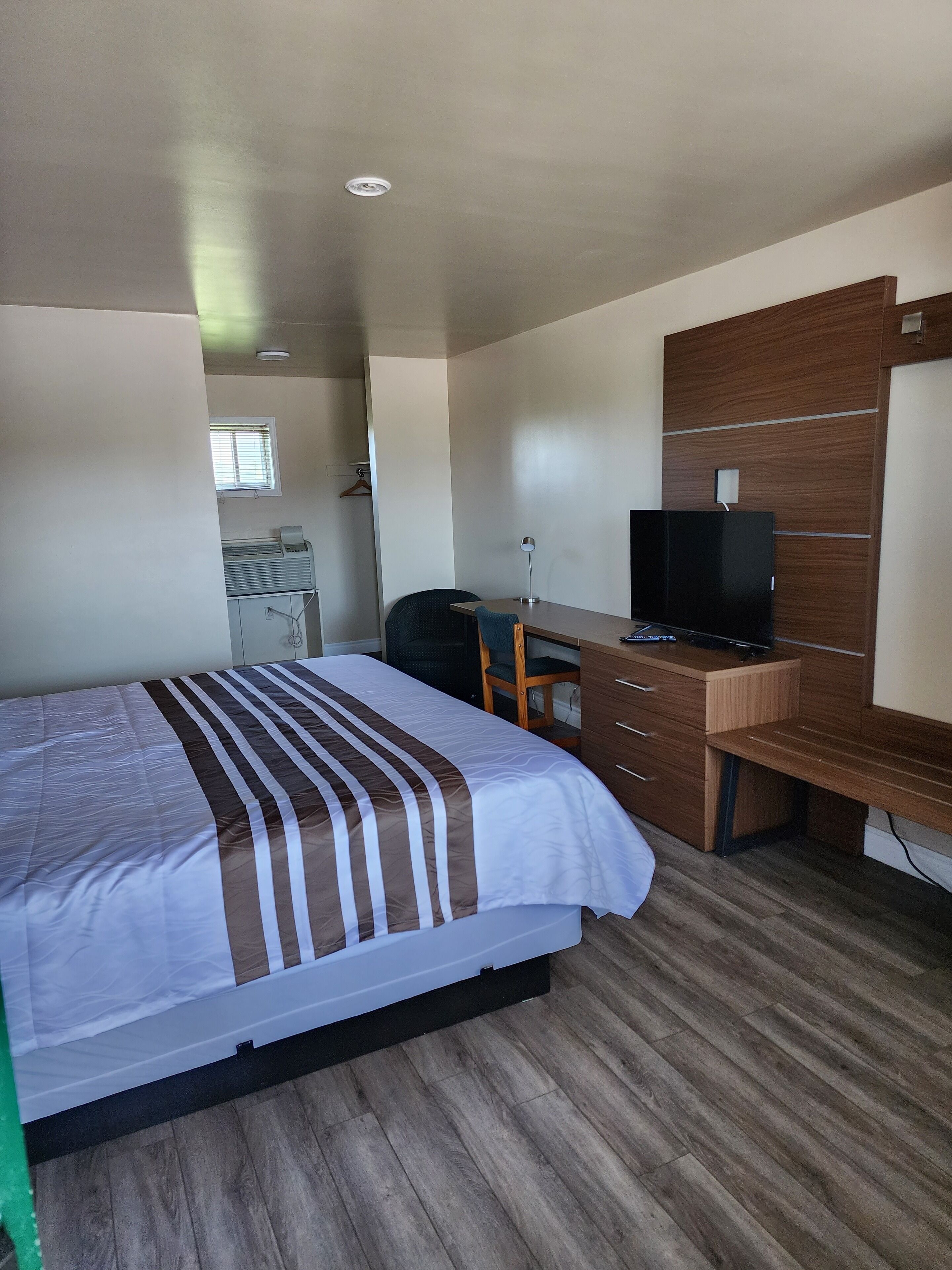 A hotel room with a bed, a desk with a television, a chair, and a window.