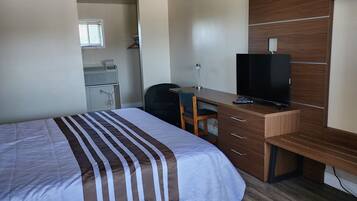 A hotel room with a bed, a desk with a television, a chair, and a window.