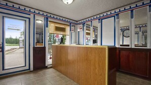 A reception area with a wooden counter, a clock on the wall, and a view of the outside through a door. - Knights Inn Lindsay (Kawartha Lakes)