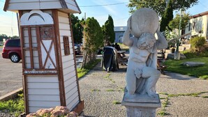 A small wooden structure with a triangular roof, a statue of a figure, and flowering plants in front. - Knights Inn Lindsay (Kawartha Lakes)