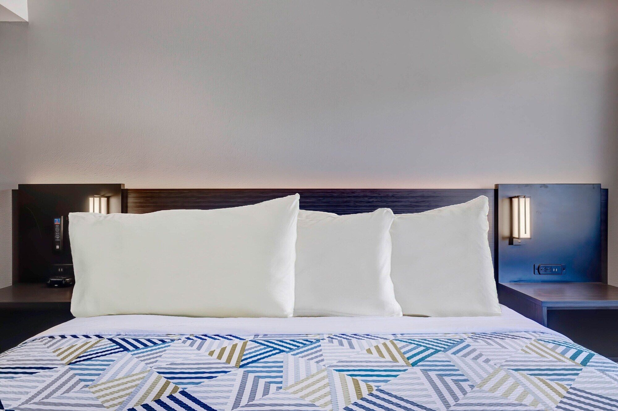 Een hotelkamer met een bed, twee kussens, een bed met een patroon erop en twee bedlampjes.