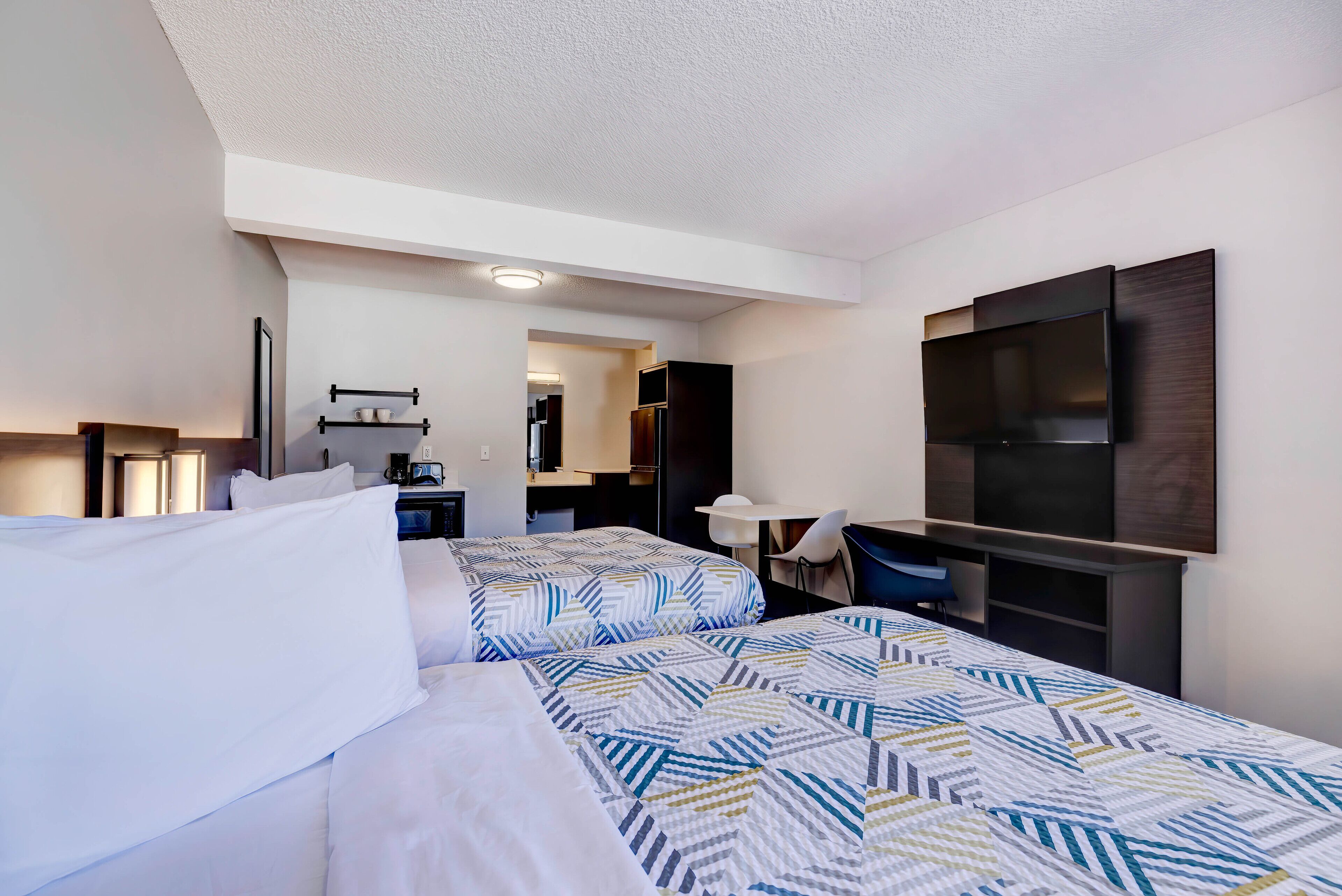 Une chambre d’hôtel avec deux lits, un bureau, un téléviseur à écran plat et une kitchenette.