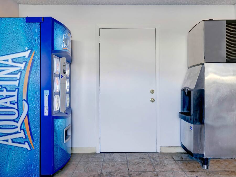 Máquina de vendas com a marca AQUAFINA, uma porta branca e um dispensador de água em aço inoxidável.