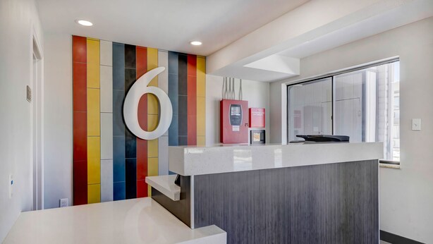 A reception area with a modern design, featuring a large number '6' on the wall, a counter with a digital kiosk, and a window providing natural light. - Studio 6 Rock Springs WY Flaming Gorge (Rock Springs)