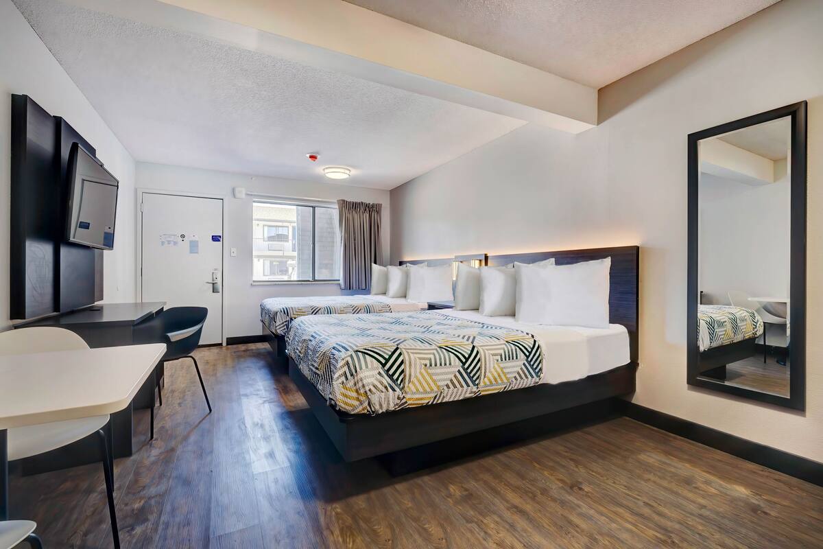 A hotel room with a bed, a desk, a chair, a television, and a large mirror.